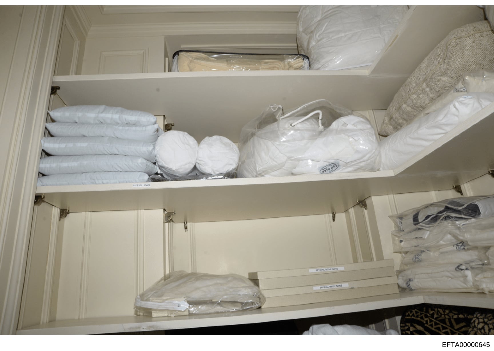 This is a photograph of an open linen closet or storage cabinet showing organized household items including folded linens, pillows, towels, and other textiles in plastic packaging. The image appears to be evidence documentation from a property search