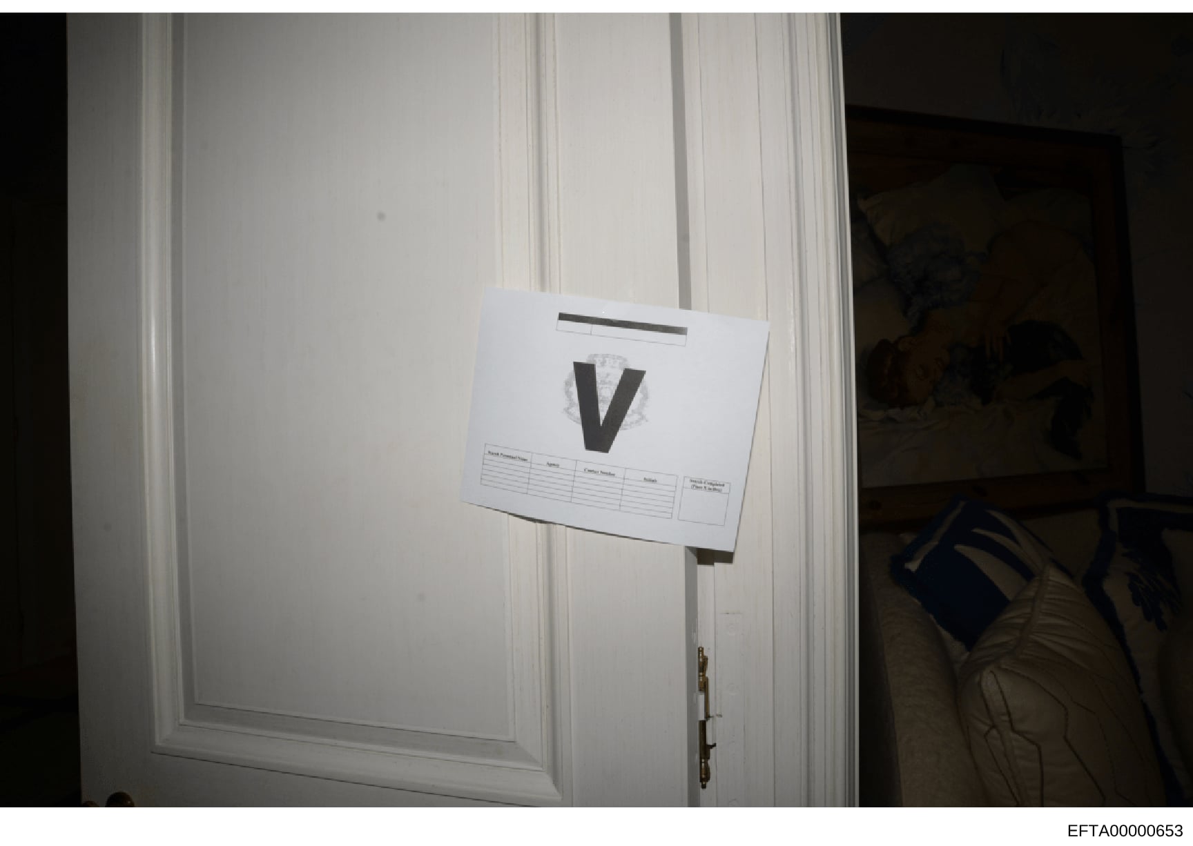 This is a forensic evidence photograph showing a white paneled door with a large black letter 'V' marker and an evidence documentation label attached. The marker and label system indicate this photo was taken as part of a systematic evidence collecti
