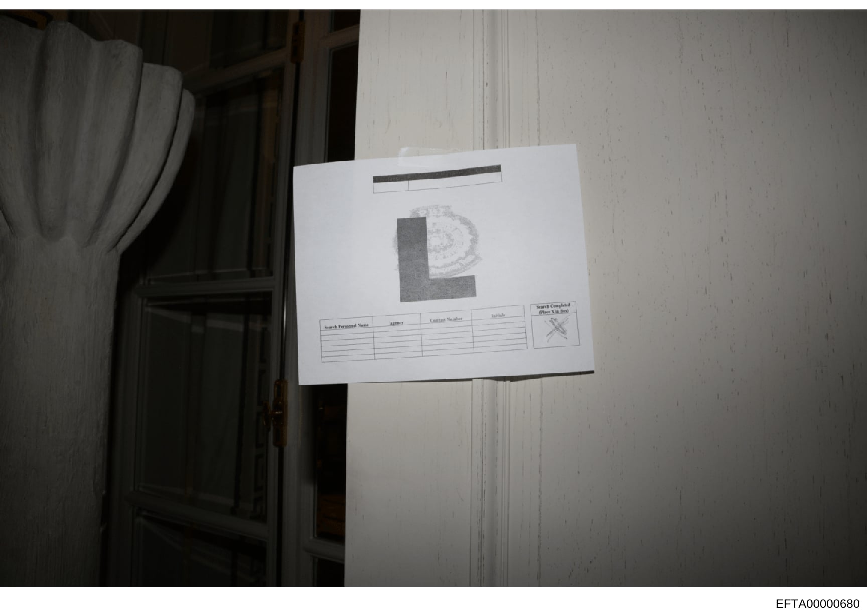 This is a photograph of an evidence documentation card or label affixed to what appears to be a white-painted interior wall or door. The card displays a large letter 'E' with an official seal or emblem, along with a data table for recording search in