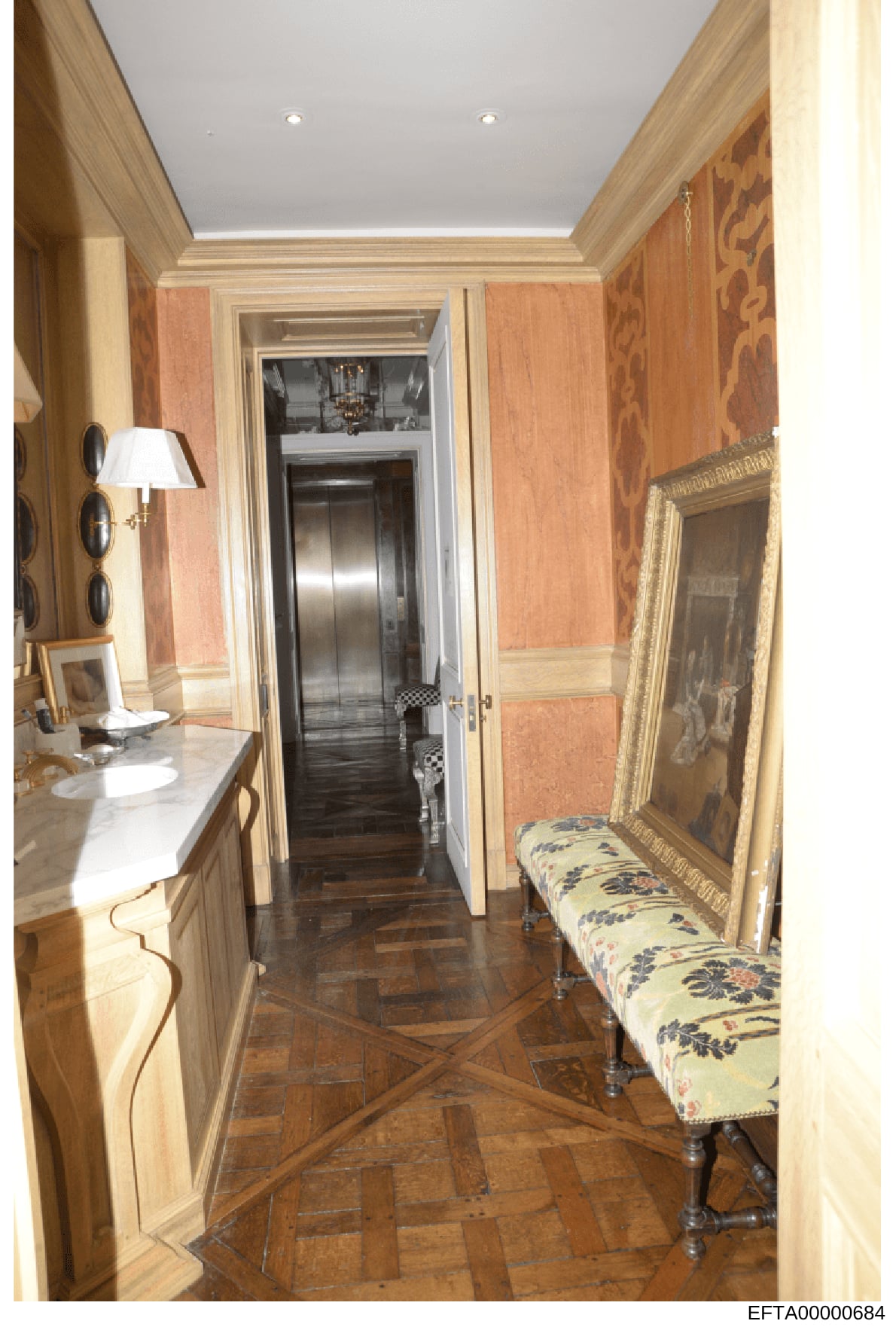 This is a photograph of an elegantly appointed hallway or corridor in what appears to be a luxury residential property, featuring custom wood paneling, decorative framed artwork, an upholstered bench, a table lamp, and a private elevator. The space r