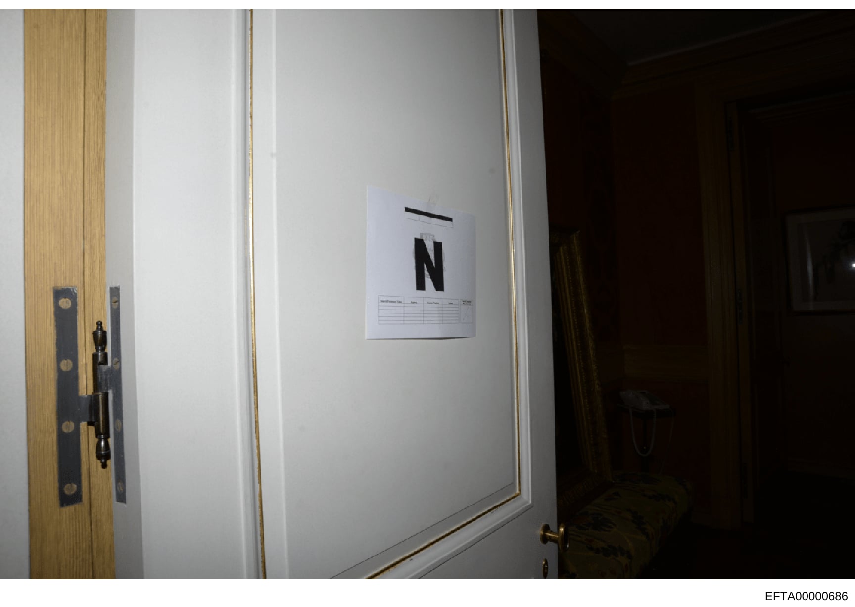 This is an evidence photograph showing an interior doorway with a white evidence marker displaying the letter 'N' attached to the wall. The marker includes a scale and reference grid used in forensic documentation. The photo appears to be taken durin