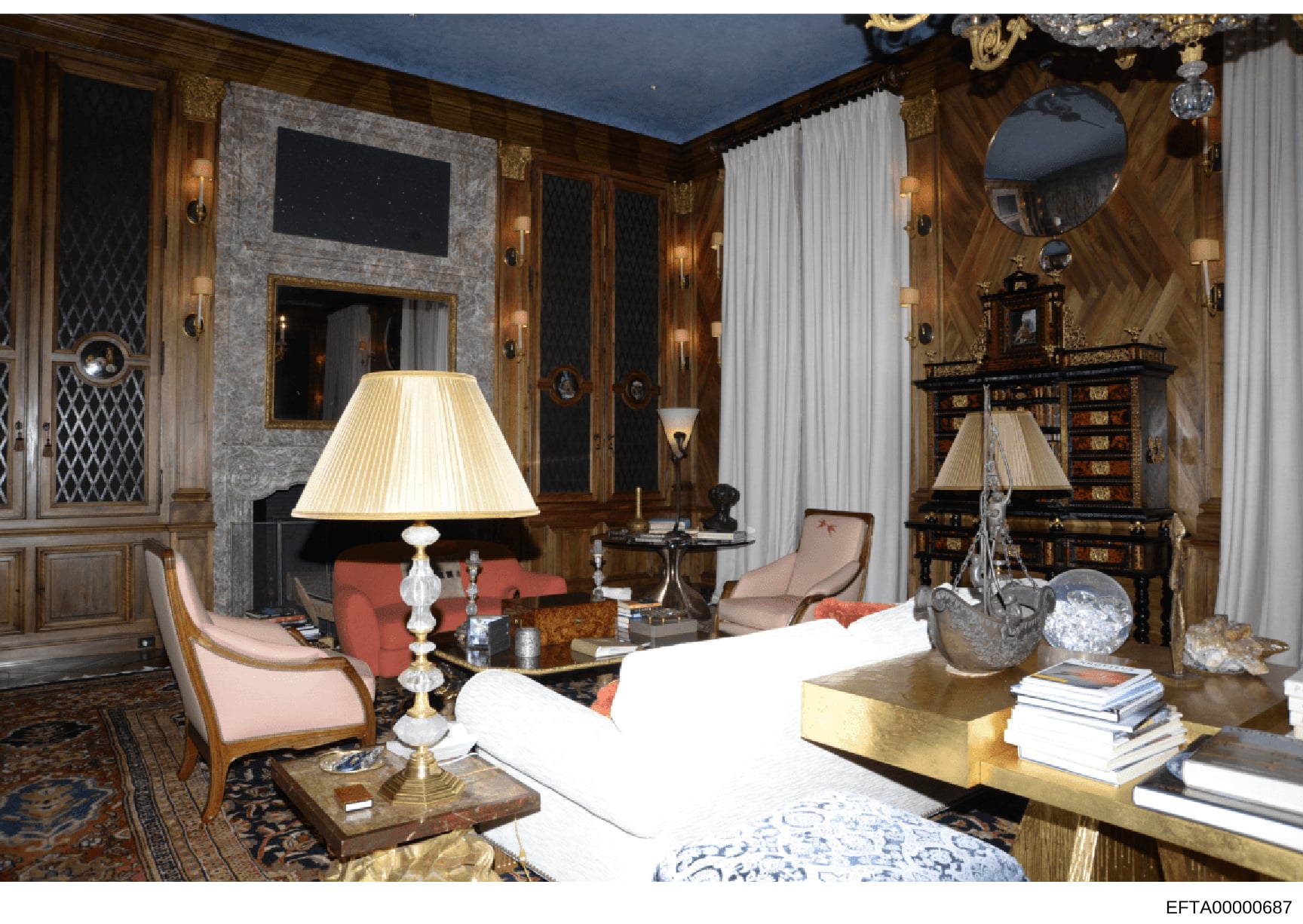 This is a photograph of an elegantly appointed formal living room featuring high-end furniture, artwork, and decorative elements. The space showcases wood paneling, a fireplace with ornate mantelpiece, designer furniture in neutral tones, and extensi