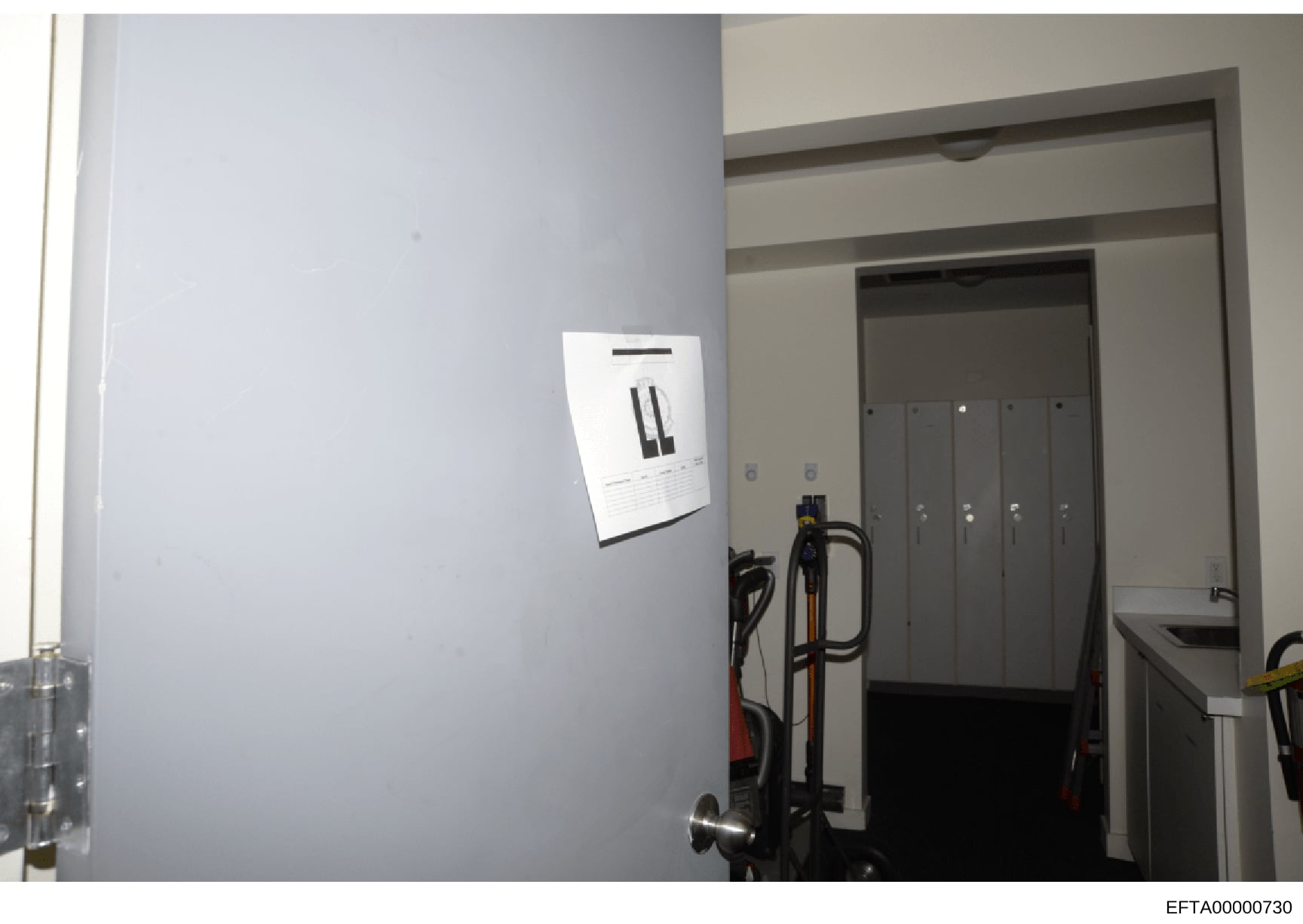 This photograph shows the interior of a room or utility space, featuring a mounted security or access control panel on a light gray wall, along with stored equipment including what appears to be exercise or maintenance equipment. The image provides d