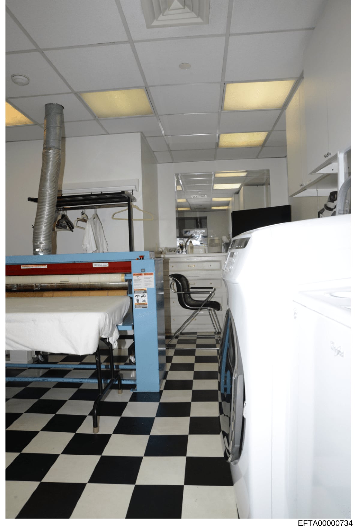 This is a photograph of a laundry room or commercial cleaning facility, showing industrial equipment including a large roller/pressing machine on the left side with white linens, and various laundry service apparatus. The room features a distinctive