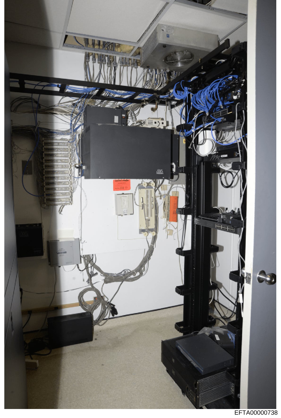 This photograph documents a utility or equipment room containing extensive electrical infrastructure, networking equipment, and cable management systems. The room shows professional-grade installation with organized cabling, power distribution panels
