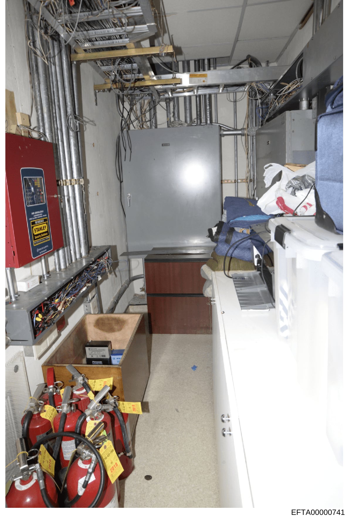 This is a photograph of an interior utility or equipment room, showing electrical infrastructure, fire safety equipment, HVAC systems, and storage areas. The image appears to be taken during a property inspection or evidence documentation process and