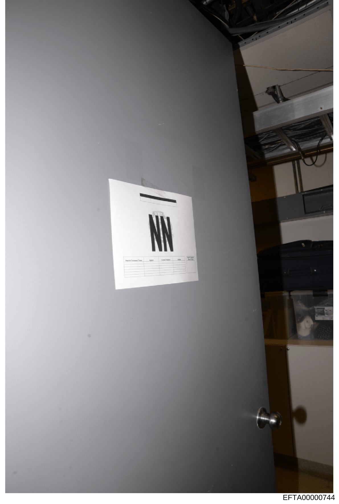 This is a photograph showing a white document or form posted on a gray interior wall, likely taken during an evidence collection or property search. The document appears to display 'NN' prominently and has a header and table structure typical of an o