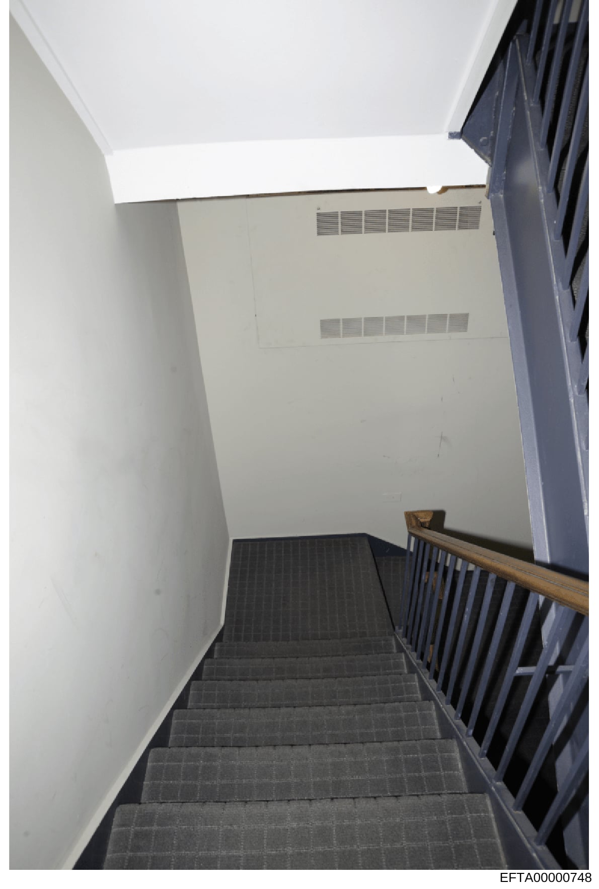This is an evidence photograph showing an interior stairwell with gray carpeted stairs, white walls, a wooden handrail, and HVAC ventilation grilles visible on the wall. The image appears to be taken from a building interior, likely from one of Epste