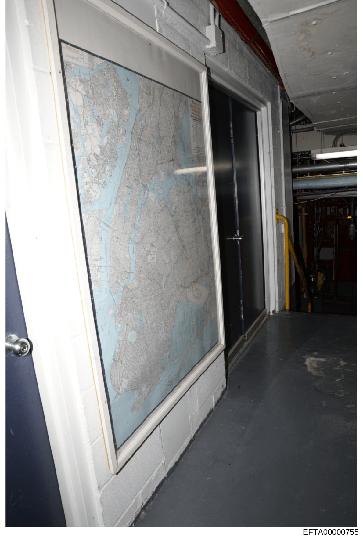 This is a photograph of a framed nautical or aeronautical chart displayed on a wall inside what appears to be an aircraft or vessel. The map shows coastal geography with blue water and gray landmass detail. The setting includes industrial or utility 