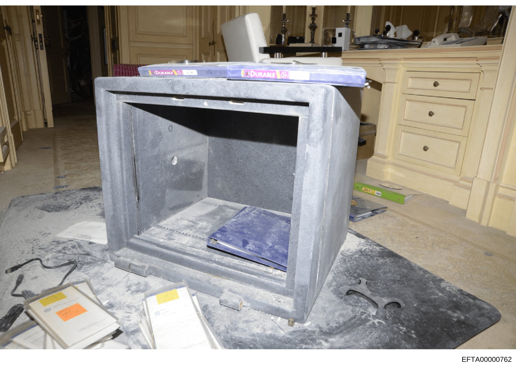 This photograph shows a large concrete or stone safe/storage unit with an open door, displaying blue folders and documents inside. The unit is positioned in what appears to be a luxurious residential interior with cream-colored cabinetry, ornate wood