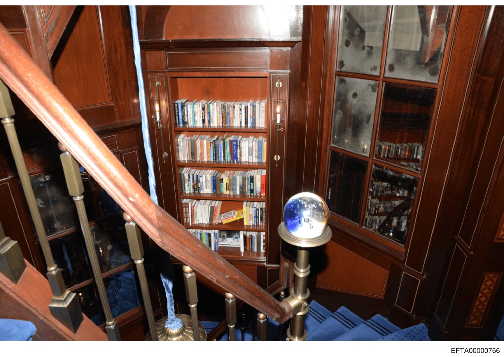 This is an evidence photograph showing the interior of a residential library or study space, featuring custom wood cabinetry with glass-fronted shelving containing DVDs and media collections, a decorative blue crystal globe on a pedestal, wooden rail