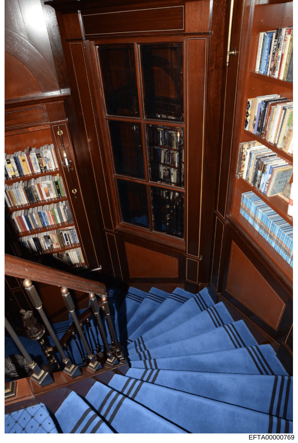 This photograph shows an interior view of what appears to be a luxury residential library or study space, featuring floor-to-ceiling wooden cabinetry with built-in bookshelves, glass-fronted display cases, and media storage. The room contains extensi