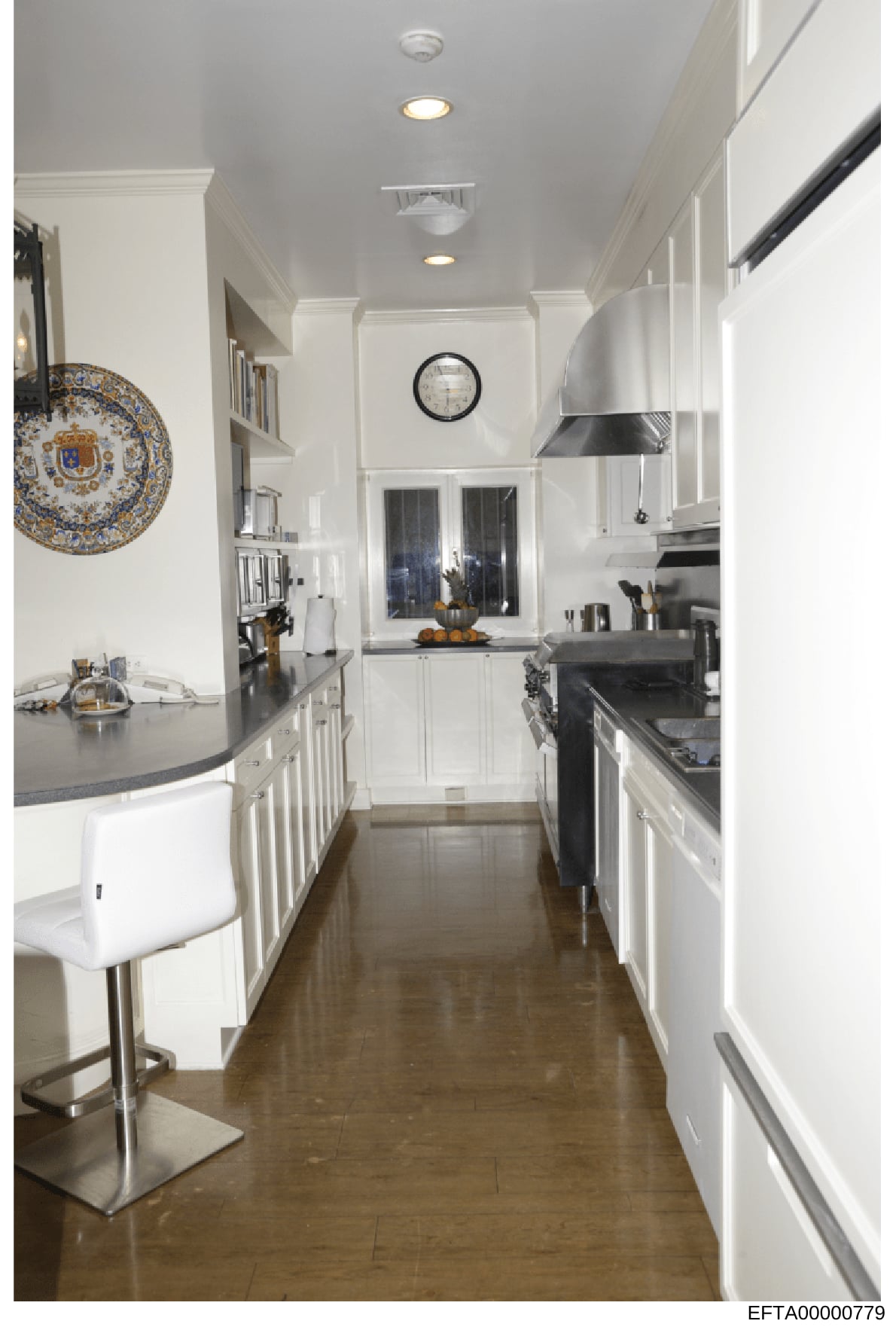 This is a photograph of a modern kitchen interior featuring white cabinetry, dark countertops, stainless steel appliances, and decorative elements including a blue and gold ornamental plate on the wall. The image appears to be documentation of a resi