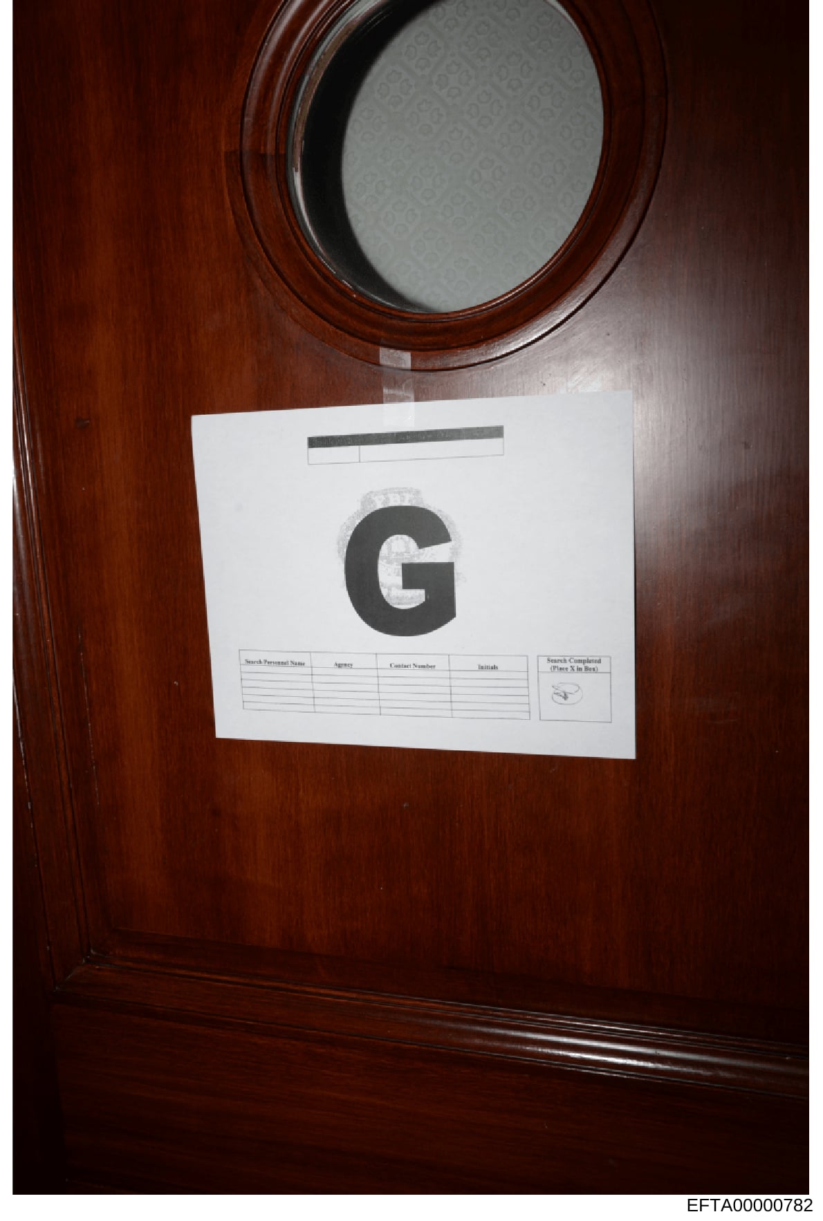 This is a photograph of a search warrant cover sheet affixed to the interior of what appears to be a wooden cabinet or door during a law enforcement search. The sheet displays a large 'G' designation and includes blank fields for recording search per