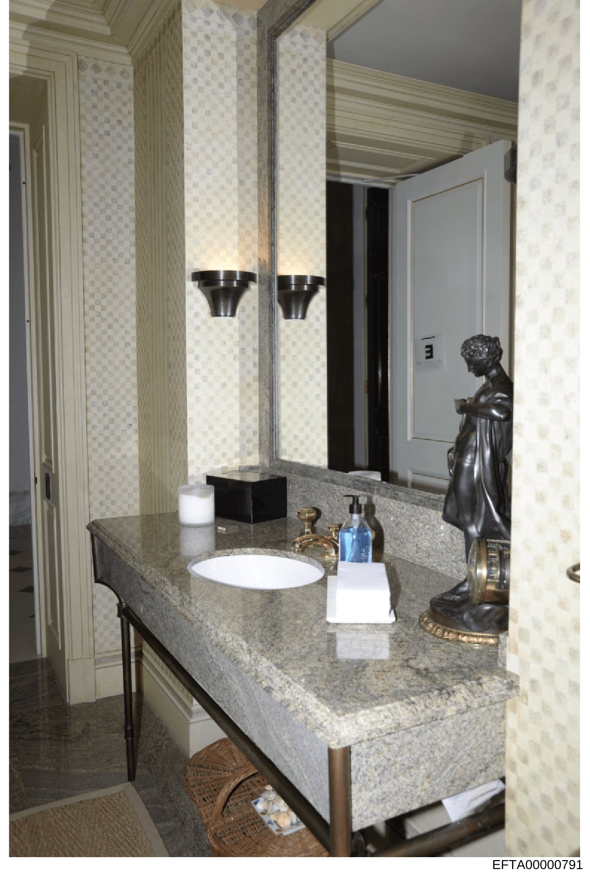 This is a photograph of a luxury bathroom interior, showing a granite countertop with an inset sink, large illuminated mirror, decorative bronze statue, and premium fixtures. The image documents the interior design and appointments of what appears to
