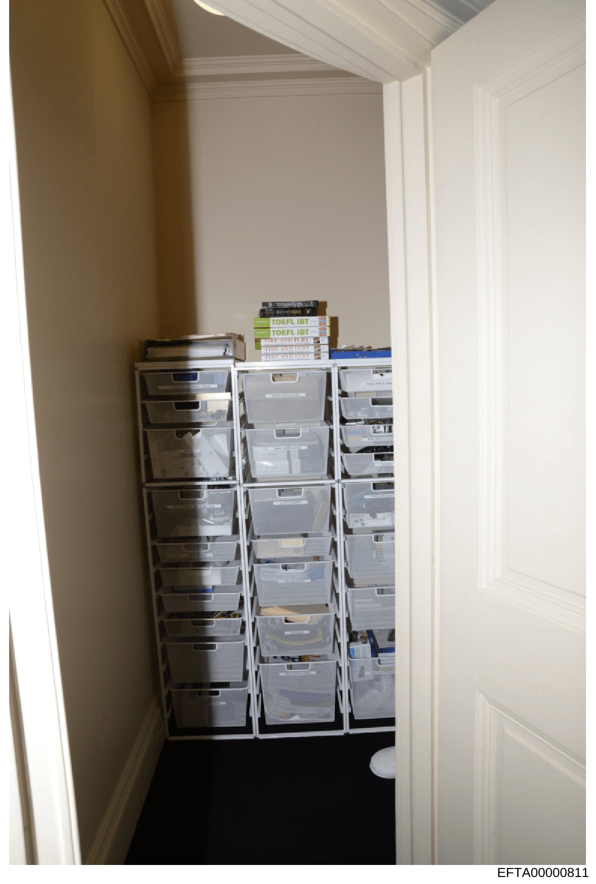 This photograph depicts a residential or office storage closet containing three large stacks of plastic filing/storage boxes organized against the walls. TOEFL IBT test preparation books are visible stacked on top of the boxes. The image appears to b