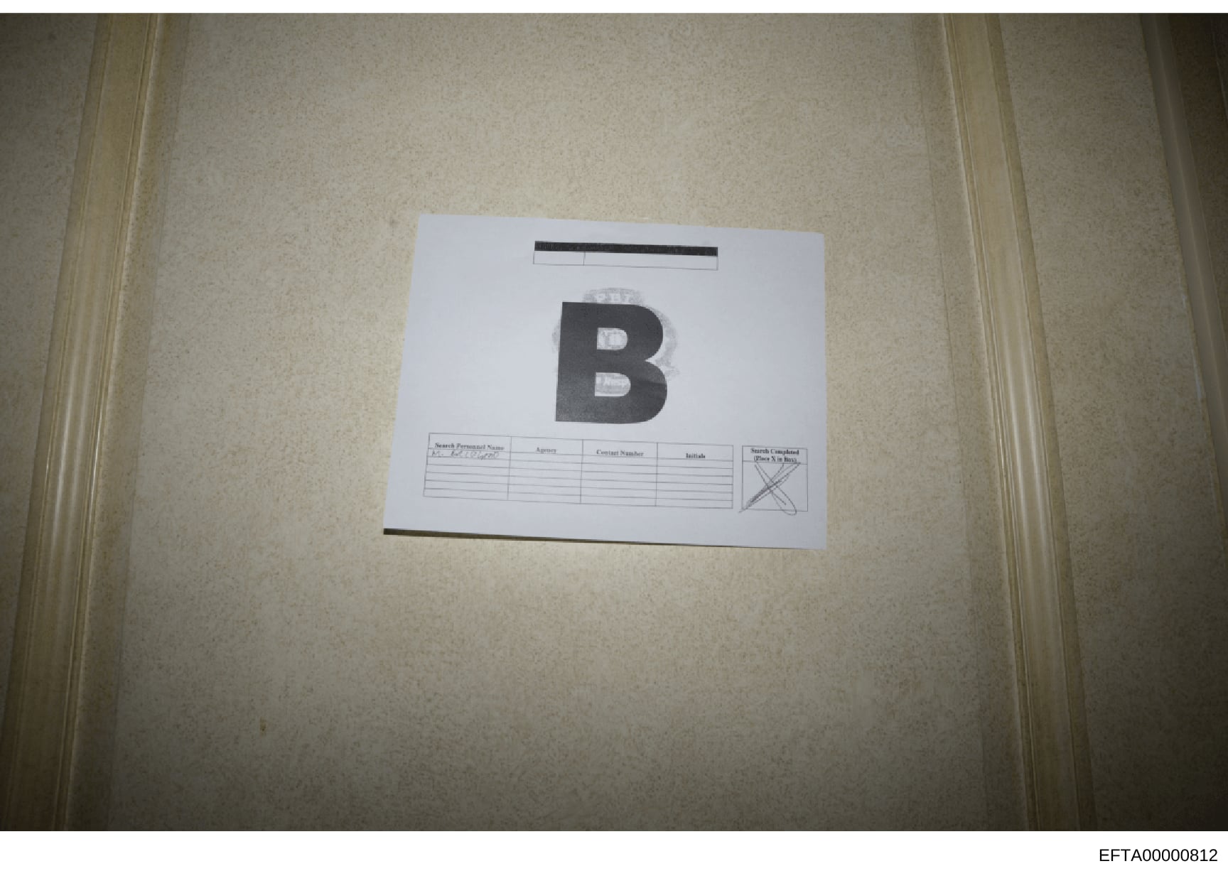 This is an evidence photograph showing a labeled item marked with the letter 'B' placed on a light-colored surface. The item includes a search personnel log form beneath it with columns for Name, Contact Number, and Initials. This appears to be part 