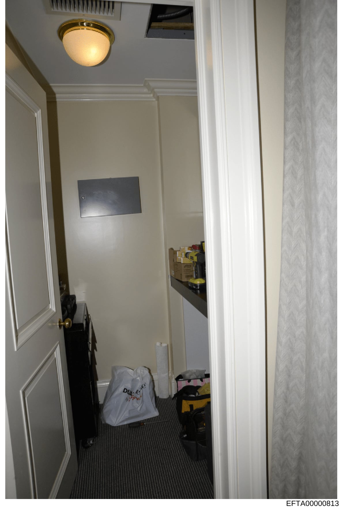 This is an evidence photograph showing the interior of a narrow hallway or utility space, likely from one of Epstein's properties. The space contains various stored items including boxes, tools, and equipment. The photograph documents the layout and 