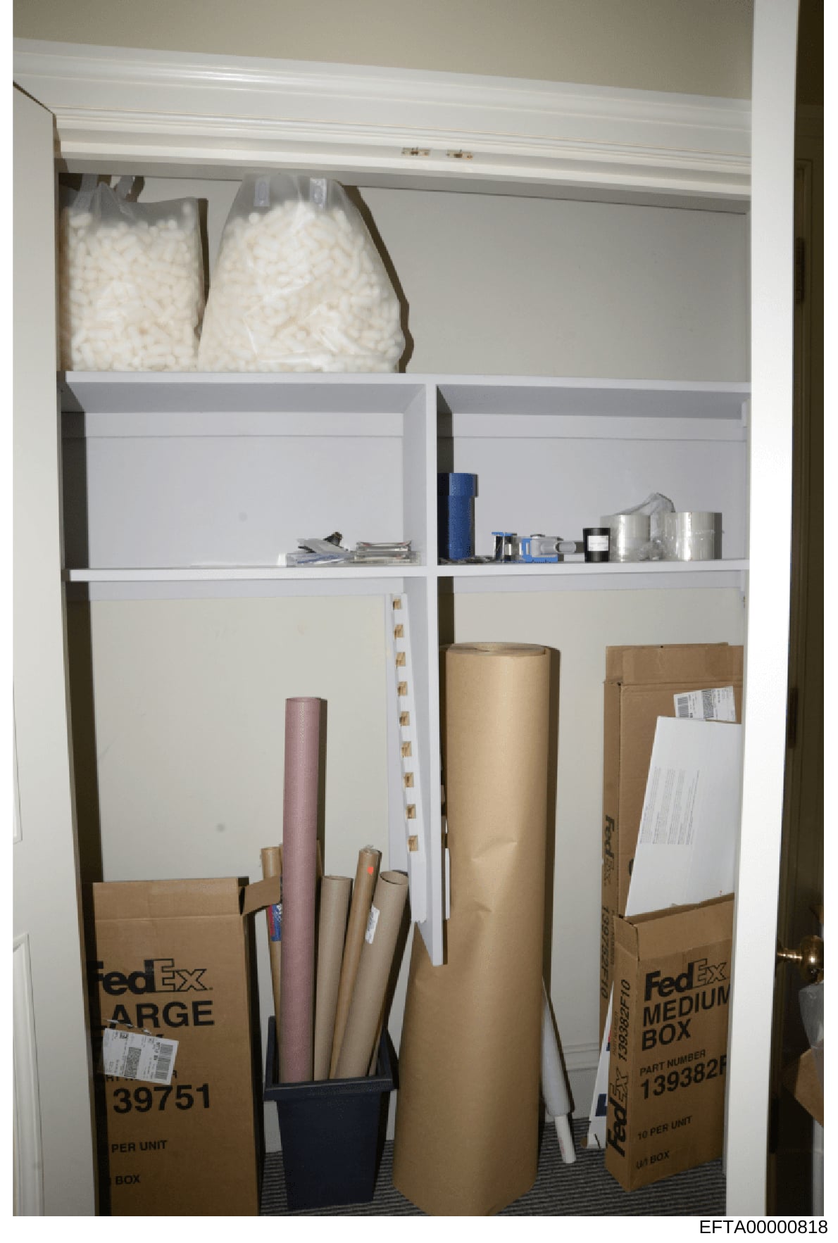 This is an evidence photograph showing the contents of a closet or storage space, featuring stacked boxes (including FedEx shipping boxes), rolls of material, bags of what appears to be packing peanuts or similar materials, and various storage contai
