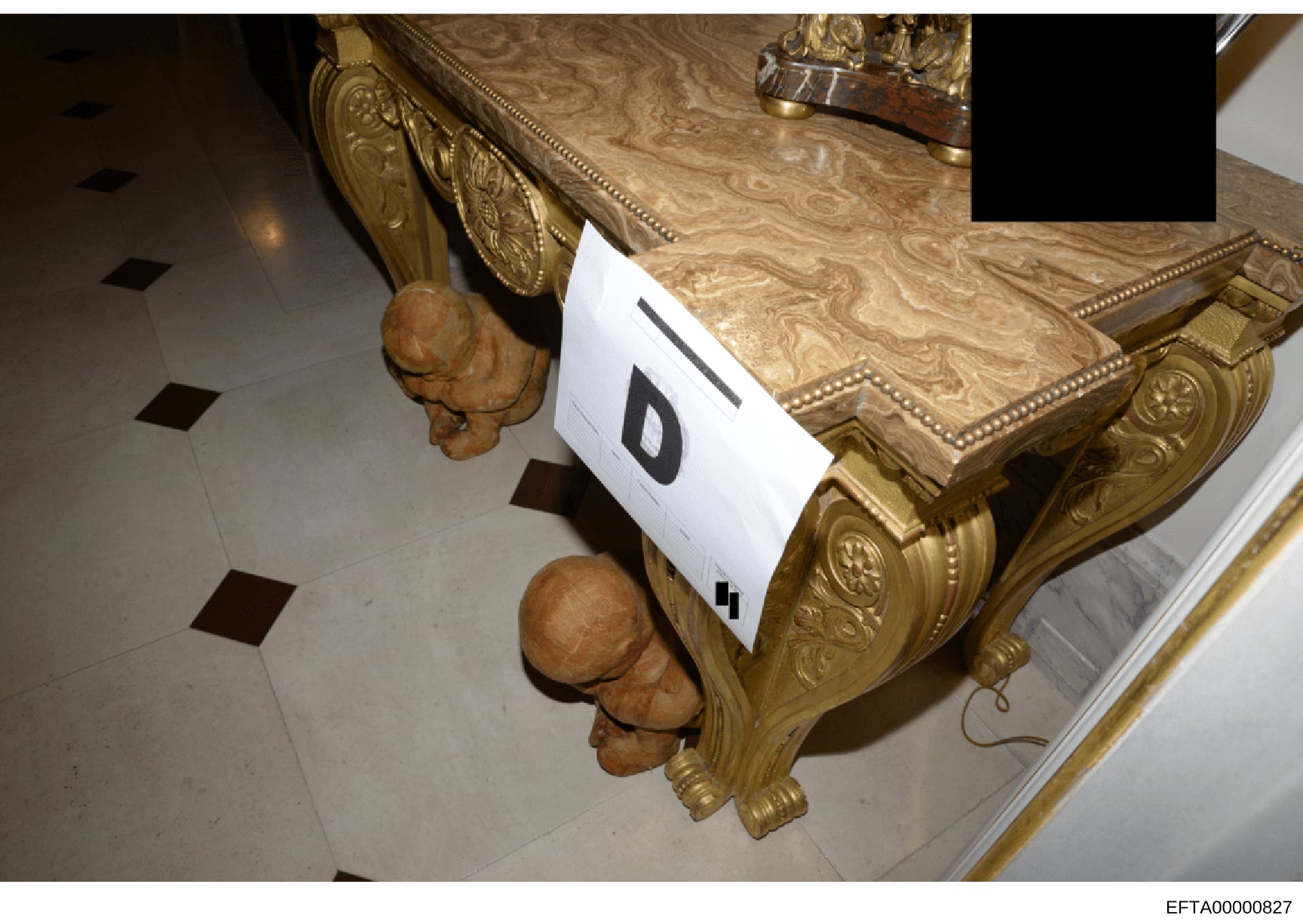 This is an overhead photograph of ornate furniture featuring elaborately carved wooden head sculptures and gilt-decorated table surfaces. The image shows evidence marking (labeled 'D') and appears to be from a property seizure or inventory documentat