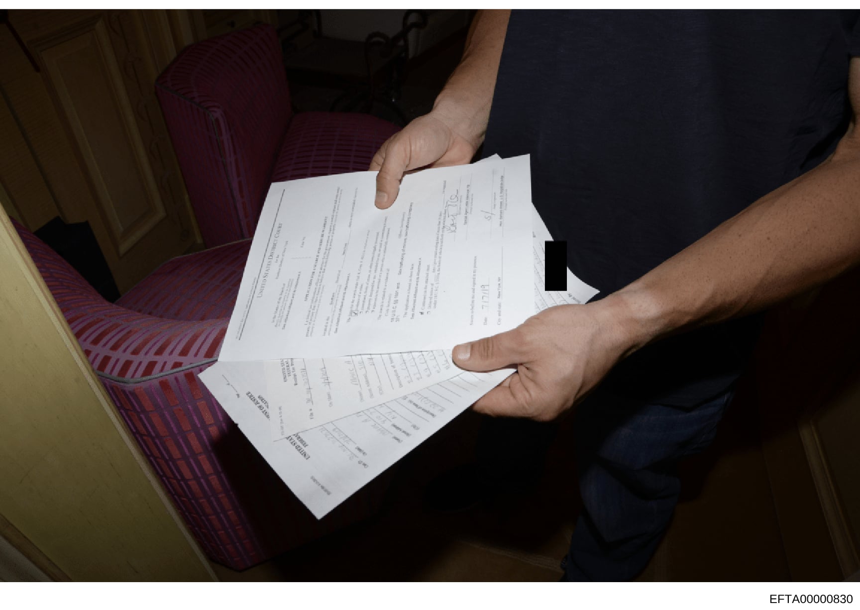 This is an evidence photograph showing multiple pages of documents being held by an unidentified person's hands. The documents appear to be investigation-related materials with text and tables visible on the pages. One section shows what appears to b