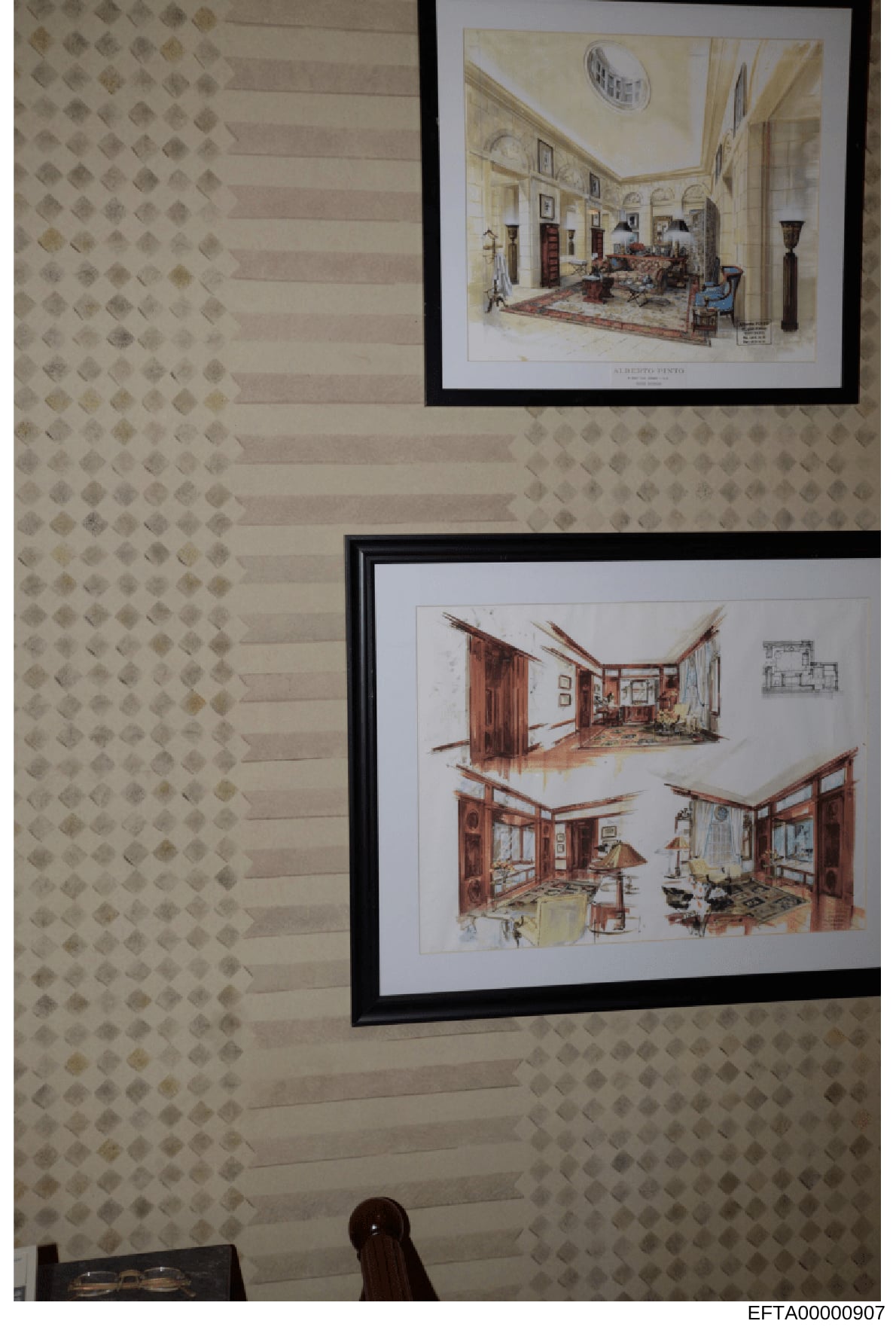 This photograph shows two framed architectural interior design renderings displayed on a patterned wallpapered wall. The renderings appear to be professional design sketches depicting elegant residential rooms with detailed furniture placement, color