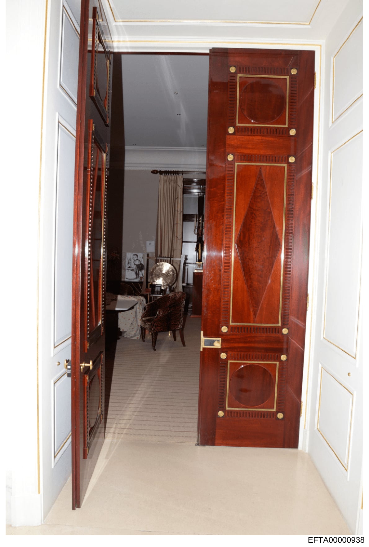 This is an evidence photograph showing the interior of a high-end residential property, depicting an entryway with ornate mahogany or similar fine wood double doors featuring inlaid panels and brass hardware. The photo captures the threshold into wha