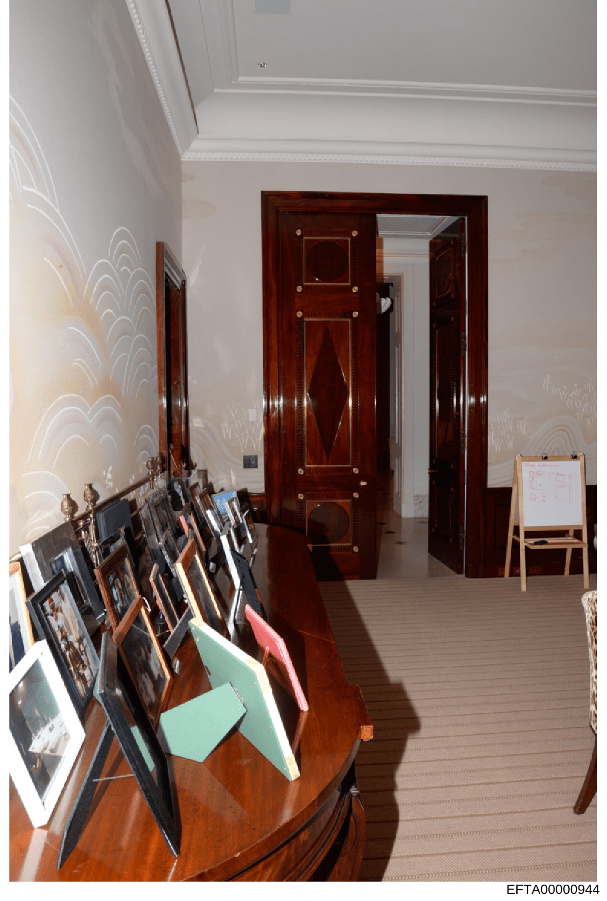 This is an evidence photograph showing an interior room with elegant furnishings and decorative elements. The image depicts a hallway or passage with dark wooden doors featuring decorative hardware, white crown molding, patterned wallpaper, and a col