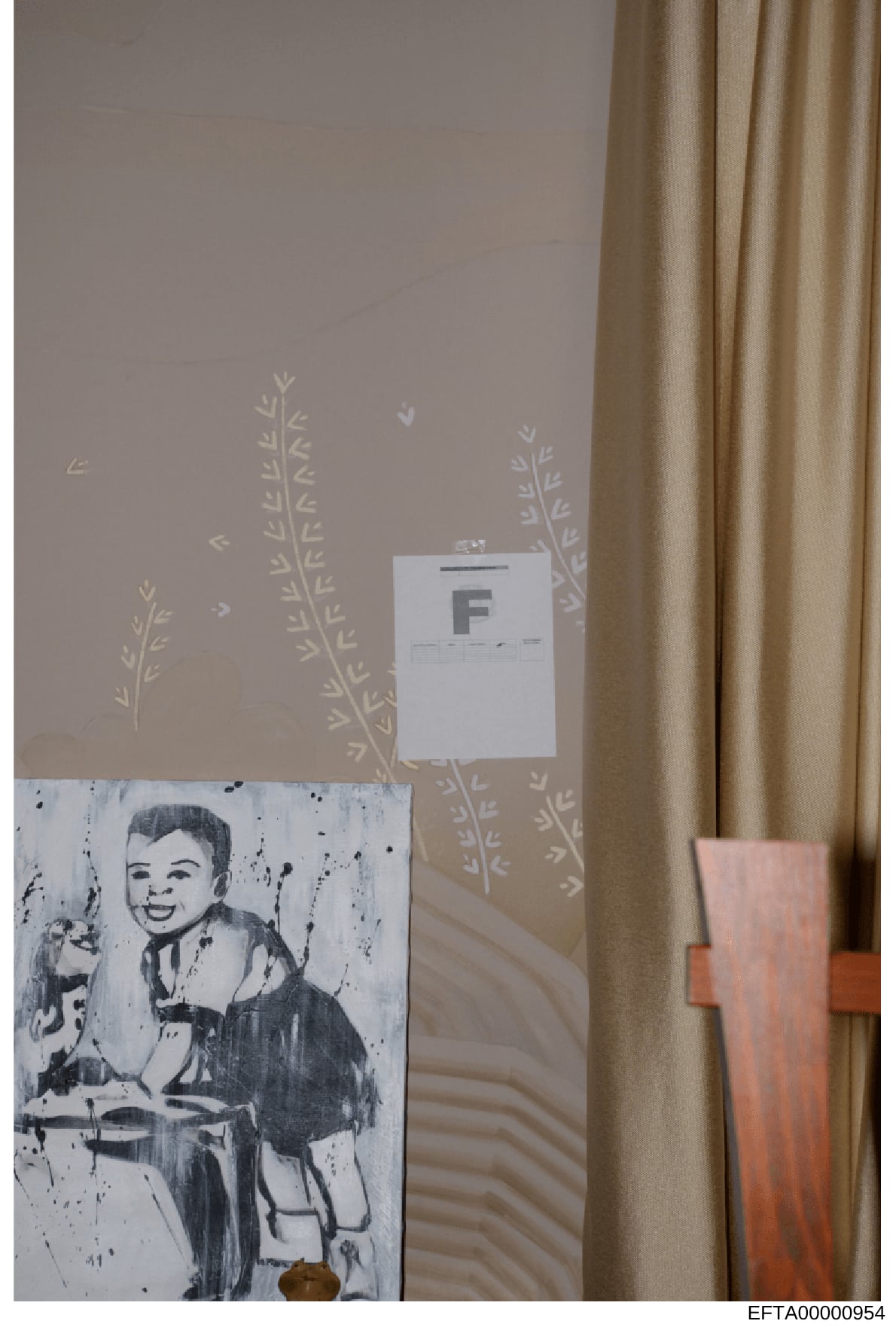 This is an evidence photograph showing an interior wall with decorative wallpaper featuring plant motifs, a tan curtain on the right, and two items: a white evidence marker labeled 'F' and what appears to be a black and white artwork or print of a sm