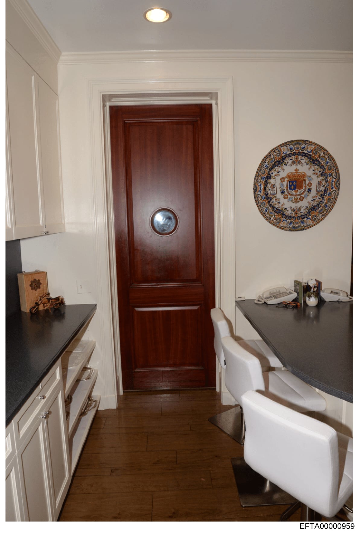 This is a photograph of an interior residential space showing a kitchen area and hallway leading to a mahogany wooden door. The image depicts the interior design and furnishings of what appears to be a property under investigation, including kitchen 