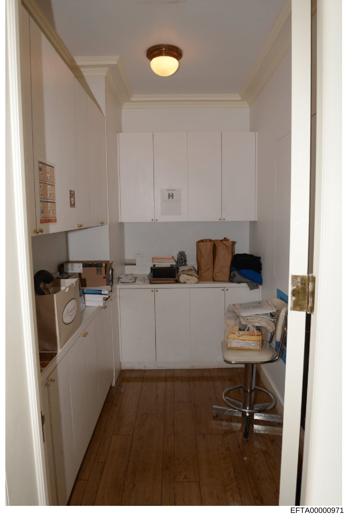 This is a photograph of a narrow utility or laundry room showing white cabinetry, a washer/dryer unit on the left side, open shelving with various household items and bags, and hardwood flooring. The image appears to be documentation of property inte