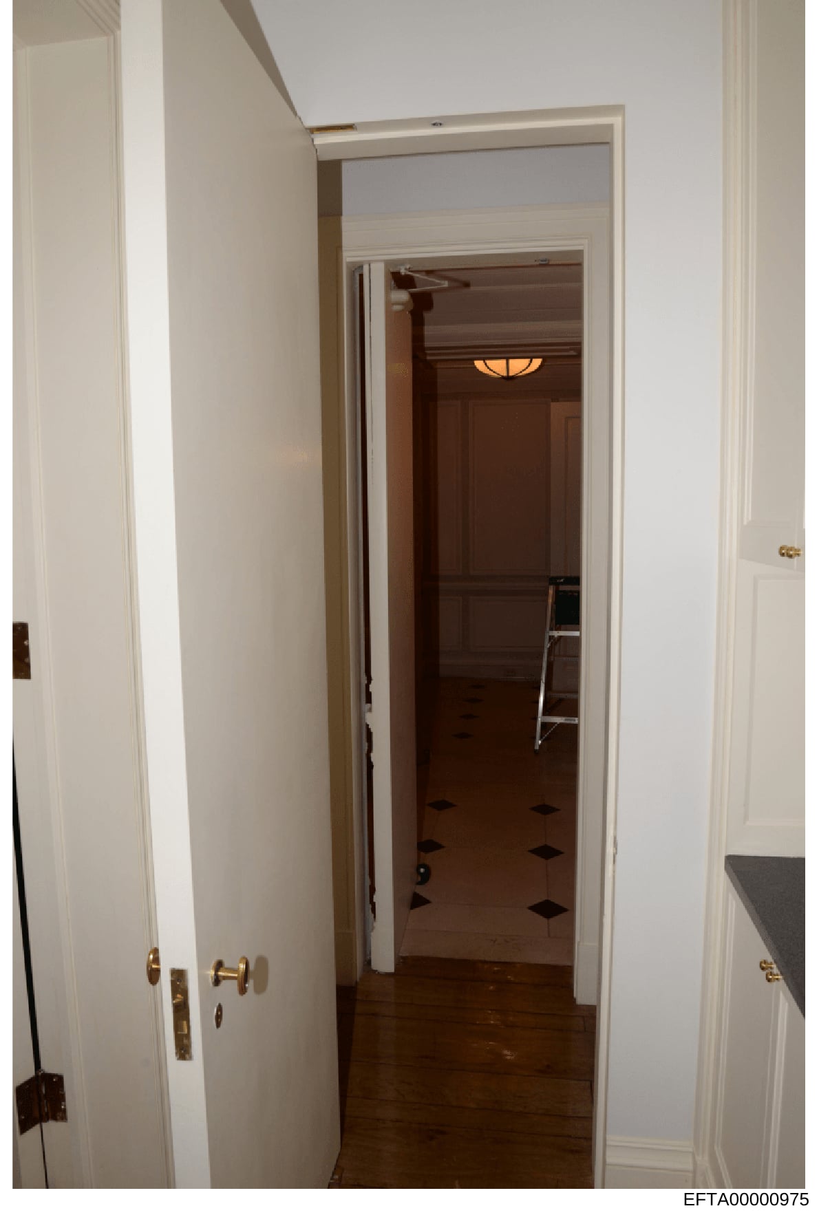 This is a photograph of an interior hallway in a residential property, showing white-painted walls, wooden flooring, multiple doorways with brass hardware, and interior lighting. The image appears to be part of evidence documentation for the investig