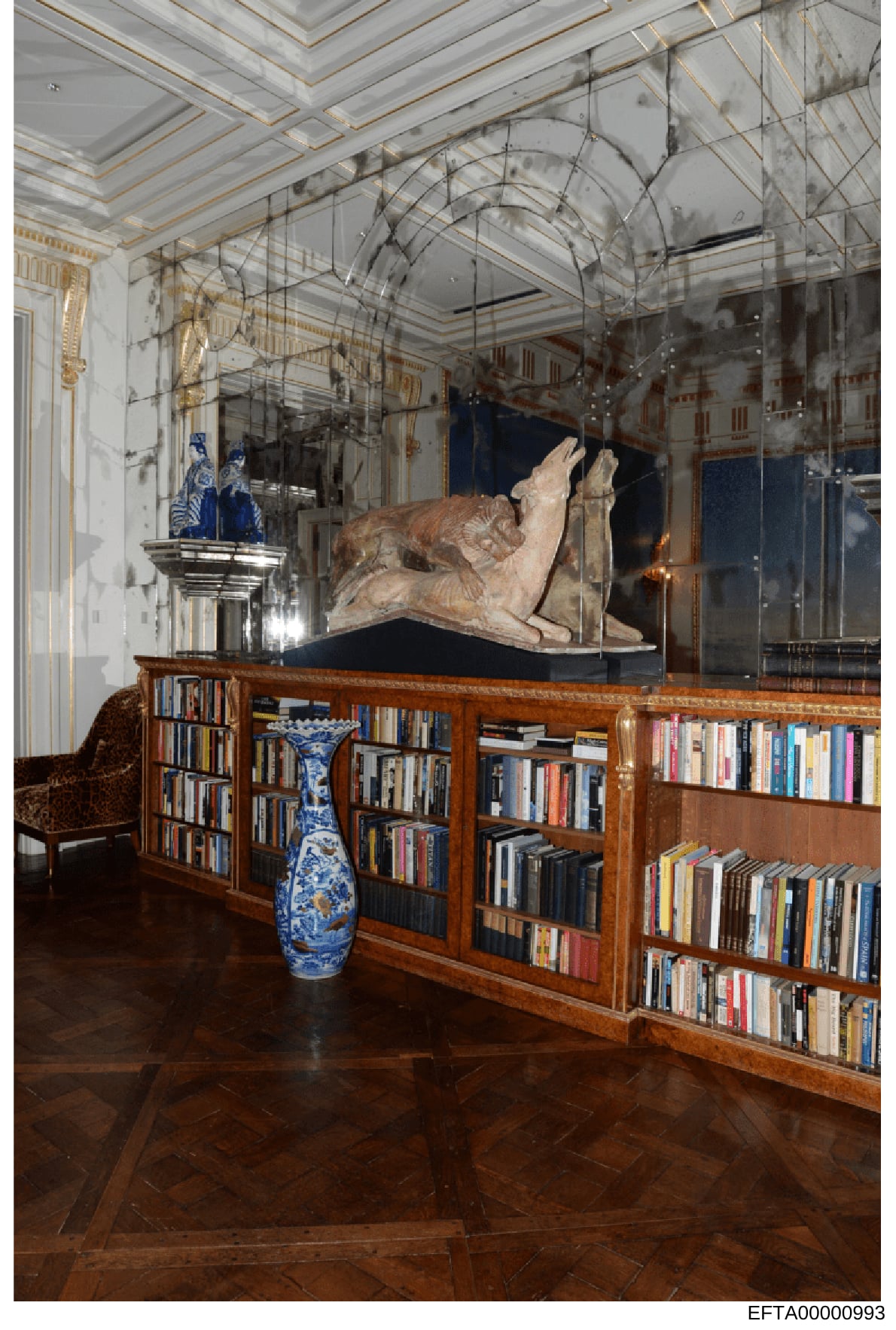 This is a photograph of an ornate interior library room featuring extensive bookshelving, fine art objects, and architectural details. The room contains a large neoclassical sculpture displayed in a glass case, blue and white decorative vases, wood p