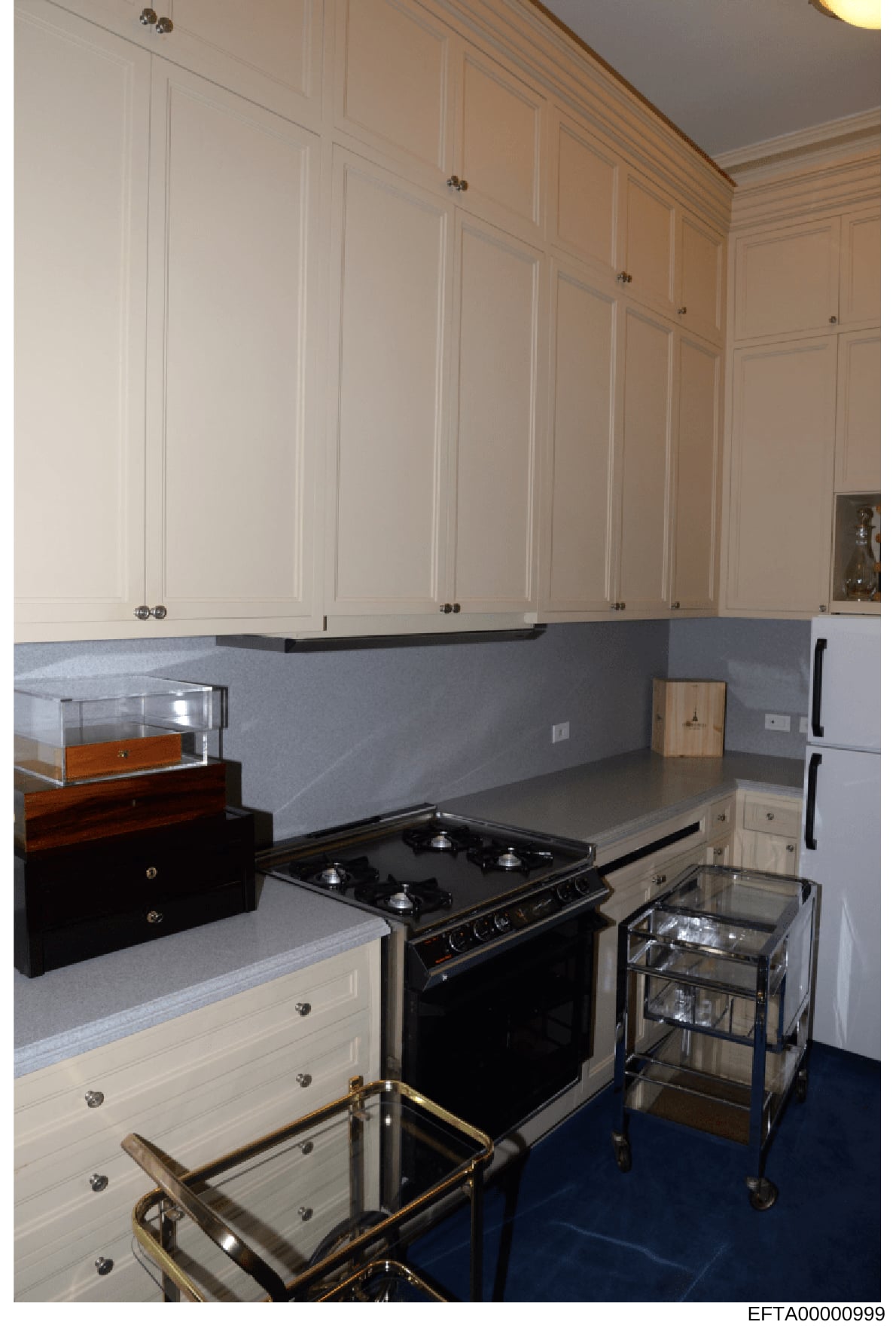 This is a photograph of a residential kitchen interior, showing custom white cabinetry, stainless steel appliances, blue-gray countertops, and decorative elements. The image appears to be documentation of property interior design or condition, likely