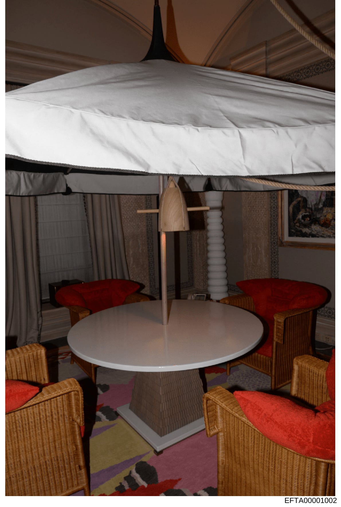 This is a photograph of a modern interior seating area under a large white canopy or tent-like ceiling structure. The room features a round white table with wicker chairs upholstered in red cushions, draped curtains in neutral tones, and decorative e