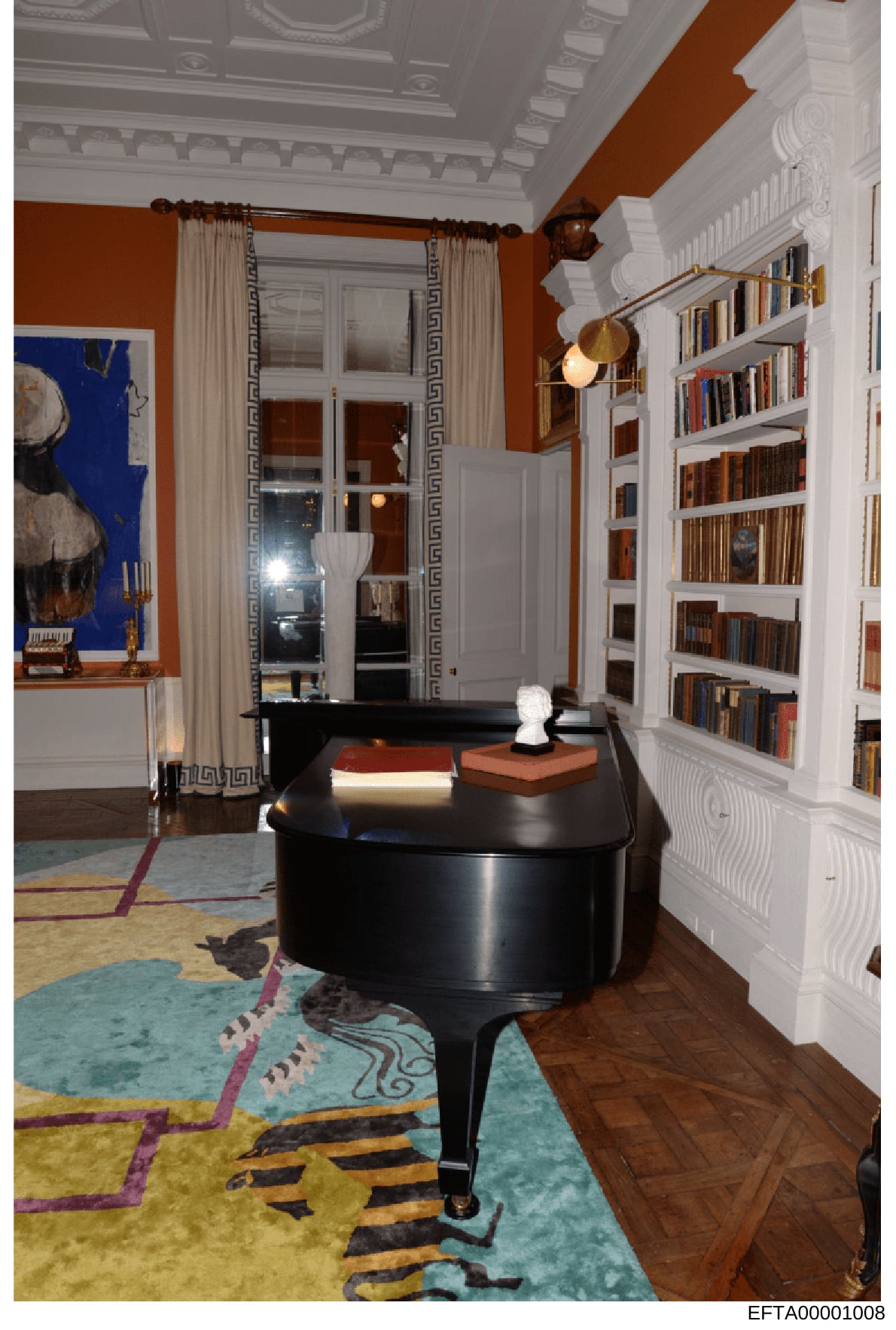 This photograph documents an elegantly appointed interior room featuring a black grand piano, extensive built-in bookshelves, and high-end furnishings. The space displays rust and white color scheme with classical architectural details including orna