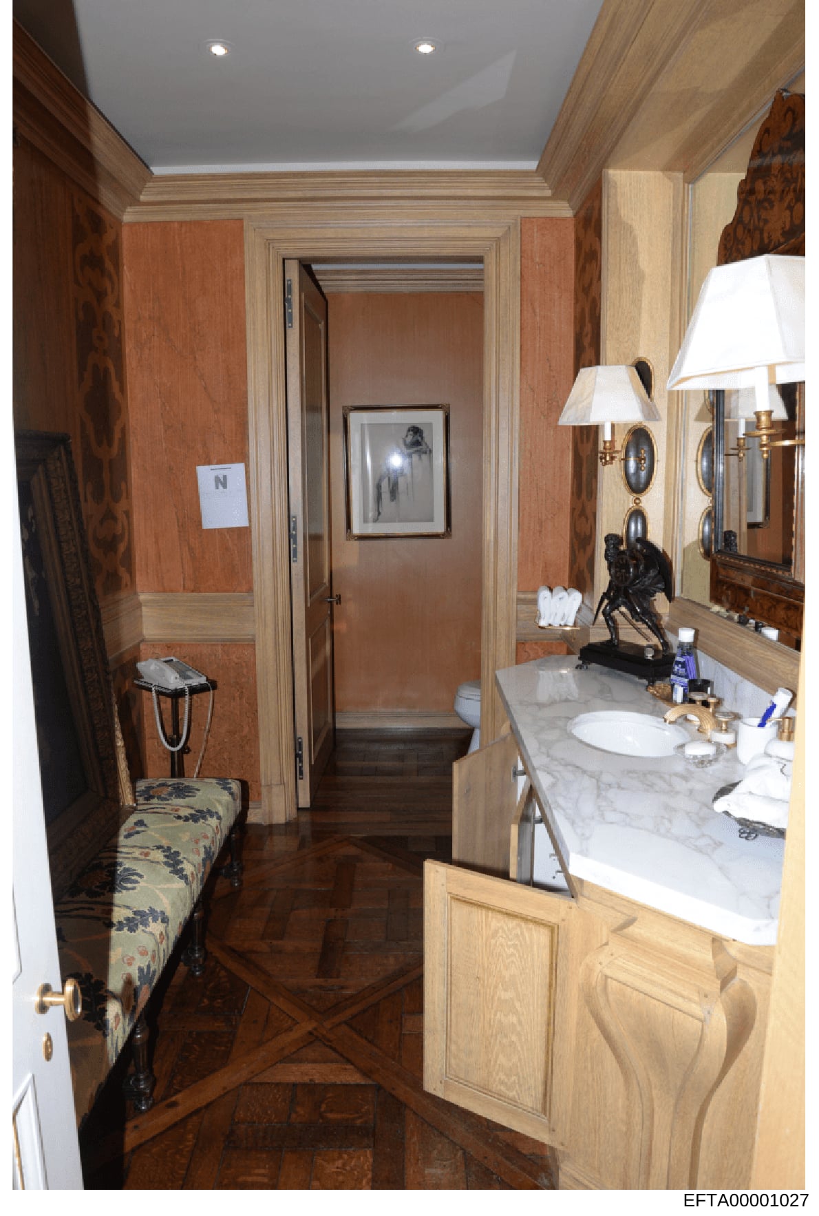 This is a photograph of an upscale residential bathroom featuring high-end finishes, marble countertops, and custom wood cabinetry. The image shows the vanity area, mirror, lighting fixtures, and an ensuite toilet room. This photograph is part of pro