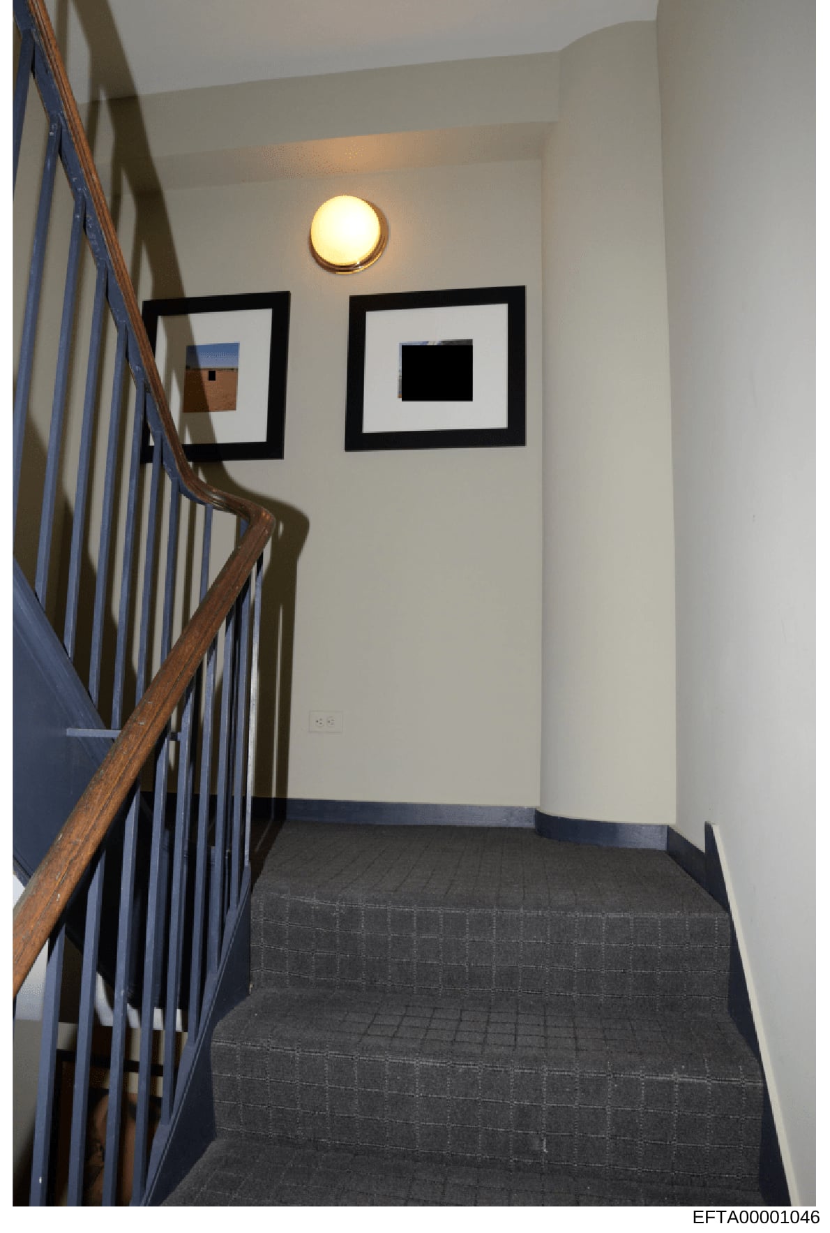 This photograph shows an interior stairwell, likely taken during a property search or evidence documentation as part of the investigation. The image captures a landing area with modern minimalist décor, including framed artwork on white walls, a circ