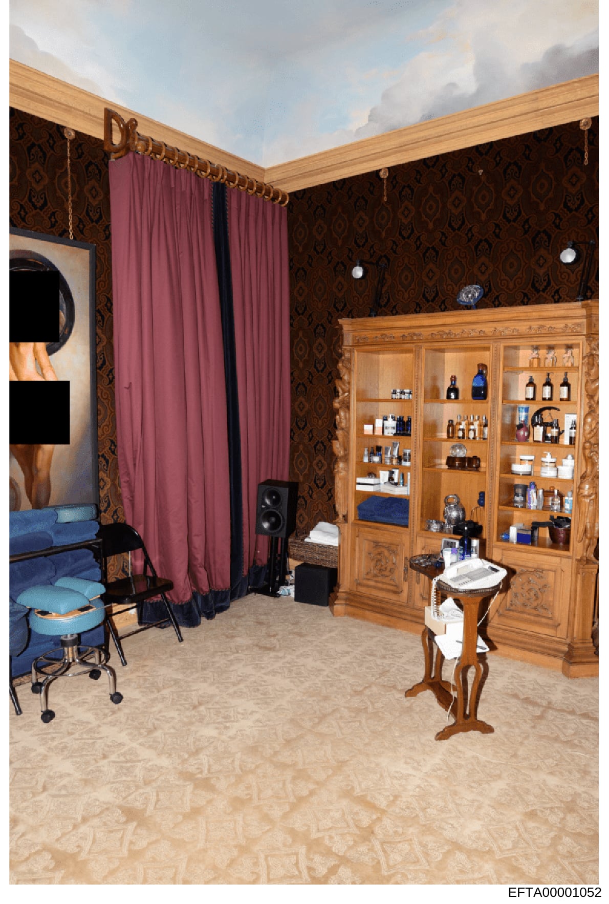 This is a photograph of an opulent interior room featuring custom wood cabinetry, wallpapered walls with ornate damask pattern, and various furnishings and personal care products. The room appears to be a luxury bedroom or spa suite, likely from one 