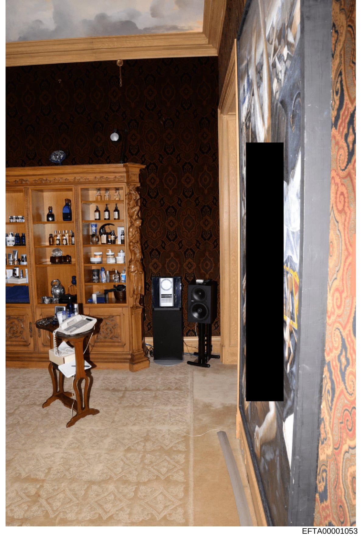This is a photograph of an interior room featuring a large wooden display cabinet with glass doors containing various bottles and luxury items, ornate dark patterned wallpaper, marble flooring, decorative furniture, and high-end audio equipment. The 