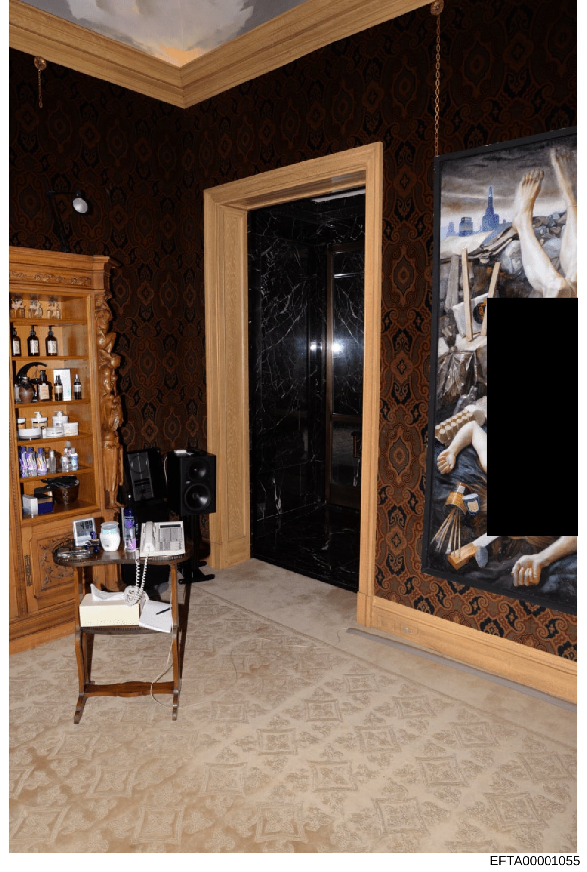 This is an evidence photograph from the Epstein investigation showing an interior room with high-end decorative elements, including dark patterned wallpaper, wooden cabinetry with glass doors containing personal care products, a black marble door fra