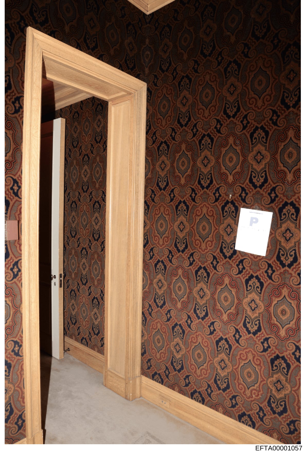 This is a photograph of an interior room space showing a wooden doorway with glass panel and decorative brown and gold patterned wallpaper. The image appears to be from an evidence collection related to one of Epstein's properties, documenting the in