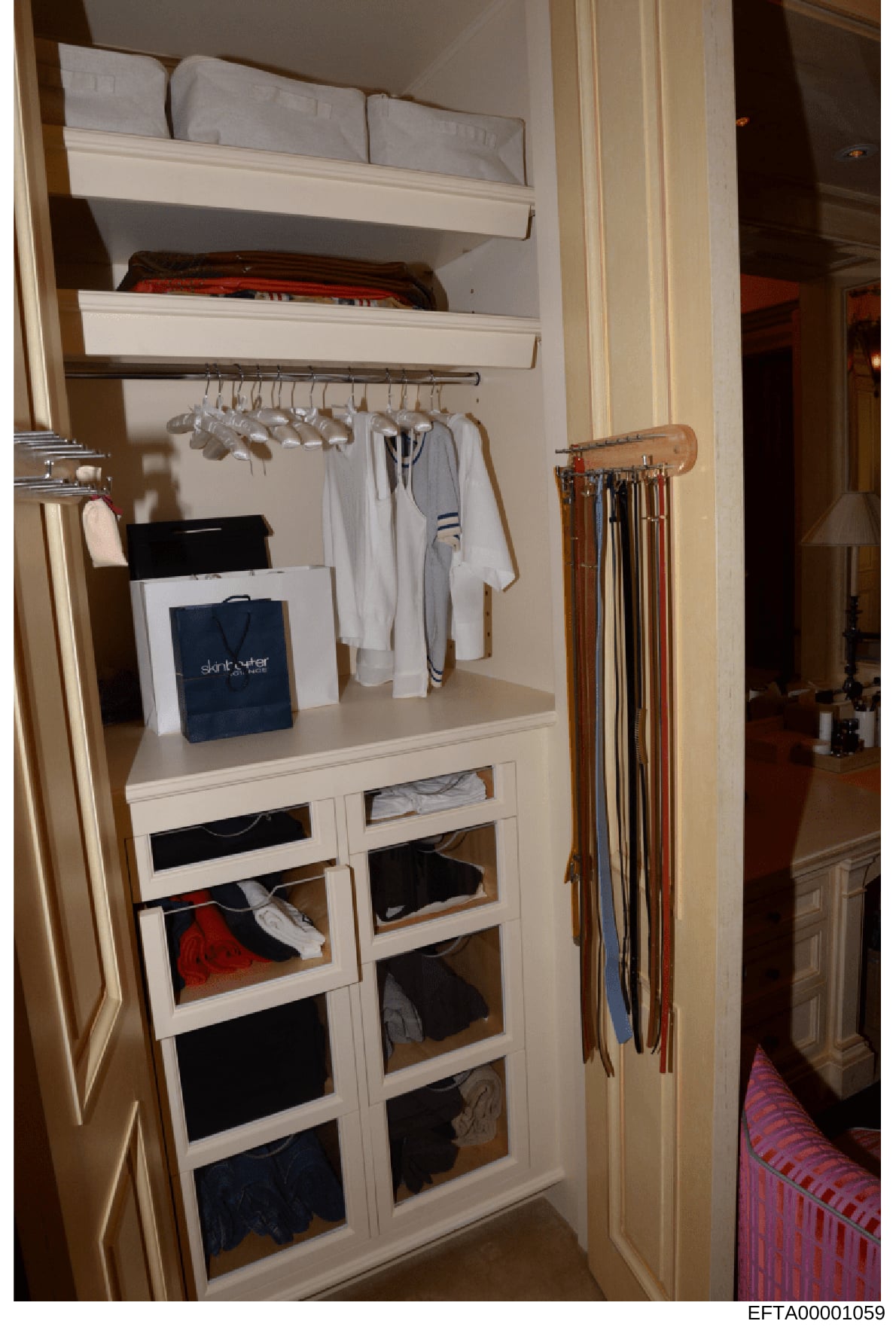 This photograph shows a built-in closet from what appears to be a residential property, displaying organized clothing storage with shelving, drawers, and hanging space. The closet contains various garments including white clothing, striped items, and
