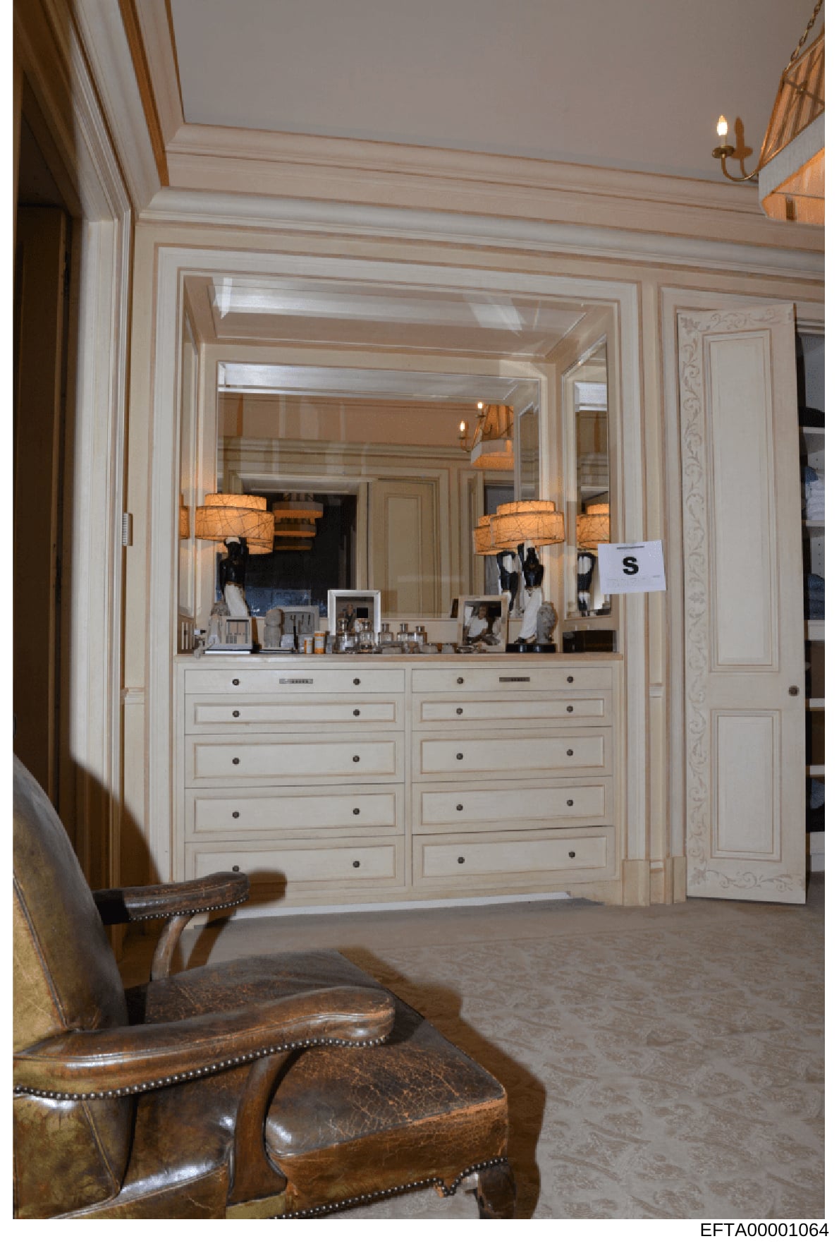 This is an evidence photograph showing the interior of a luxury bedroom, featuring a large custom-built vanity with extensive storage drawers, an oversized mirror with decorative lighting, and high-end furnishings. The photograph documents the interi