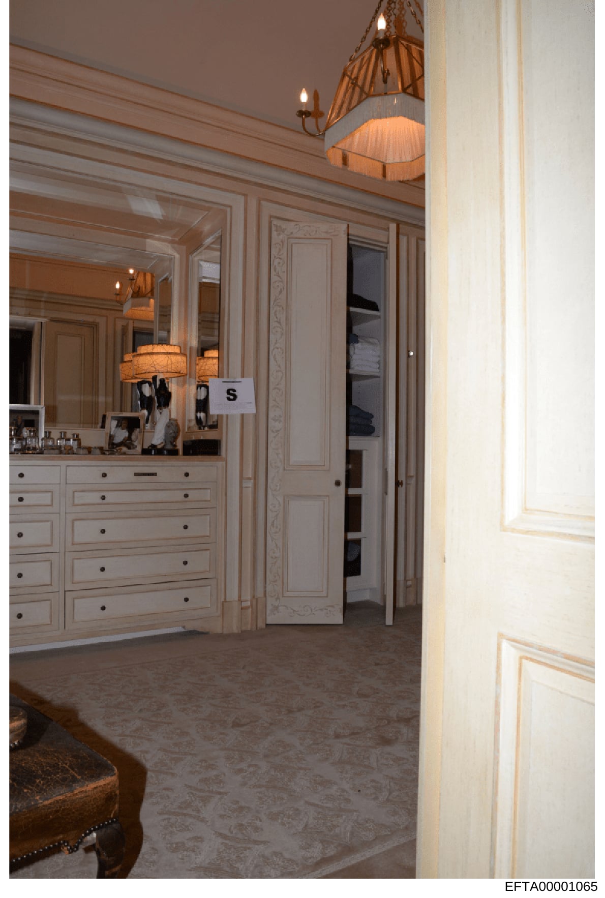This is an evidence photograph showing the interior of an upscale bedroom space, featuring a large vanity with mirror, multiple drawers, decorative lighting fixtures, and an open closet area. The image appears to be from a property belonging to or as