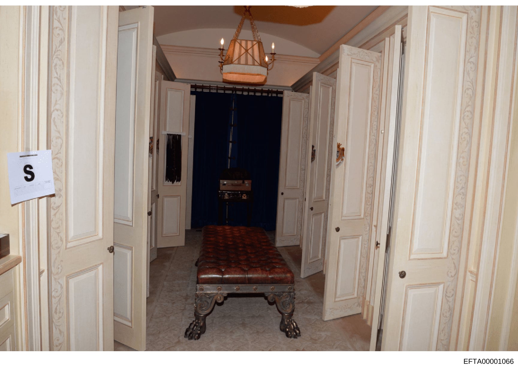 This is an evidence photograph showing an elegant residential hallway with cream-colored paneled doors, decorative molding, a leather ottoman bench with ornate claw feet, and a hanging lantern fixture. The image appears to be from one of Jeffrey Epst
