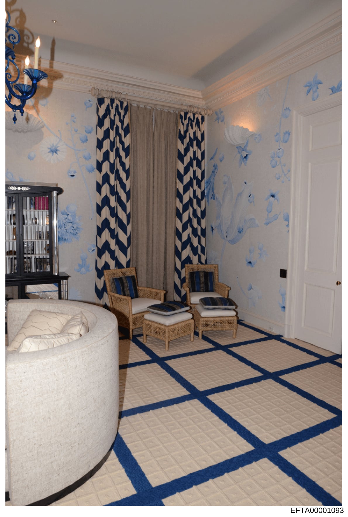 This photograph shows an elegantly decorated bedroom featuring a sophisticated color scheme of cream, white, and navy blue. The room includes a curved white upholstered bed, two wicker armchairs with navy cushions, decorative wallpaper with blue flor