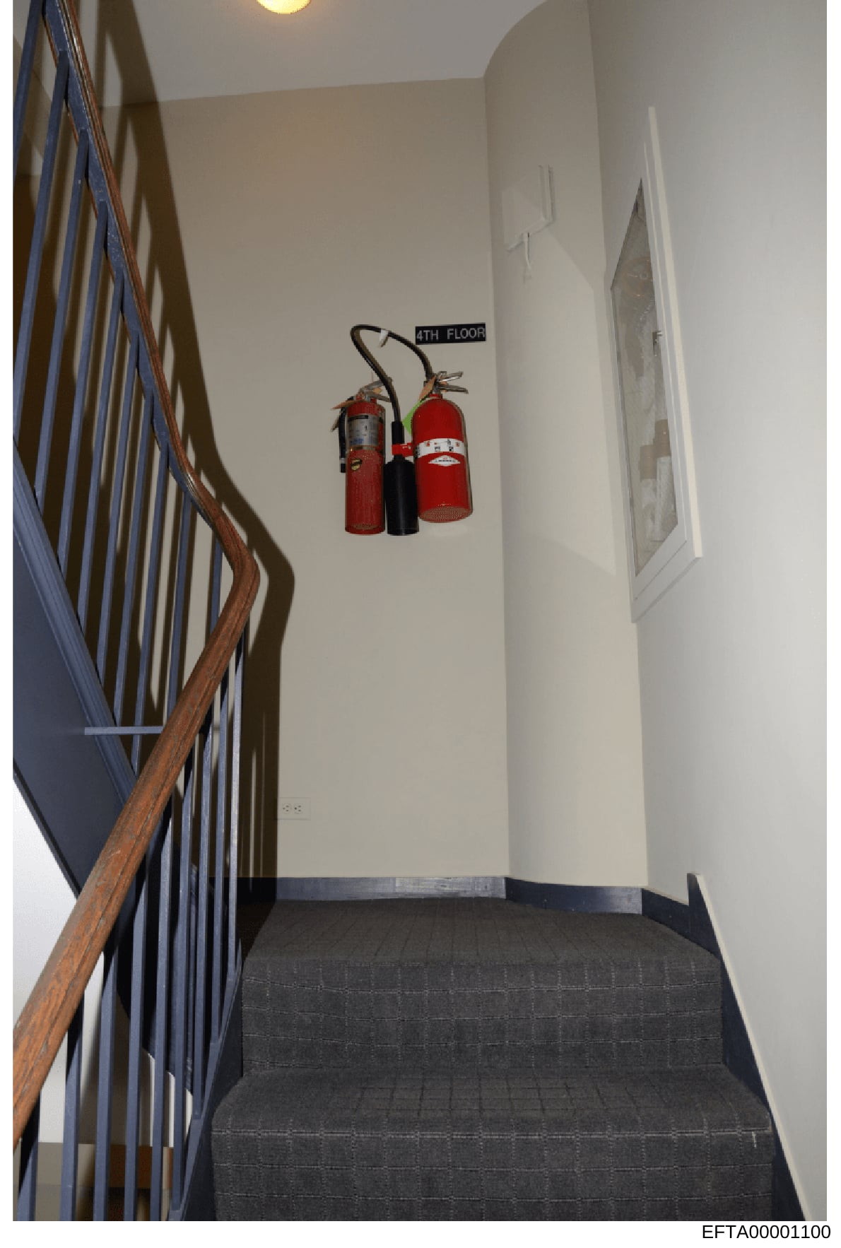 This is a photograph of an interior stairwell in a multi-story building, showing the staircase landing between floors with fire safety equipment mounted on the wall. The image captures architectural details and building safety infrastructure, likely 