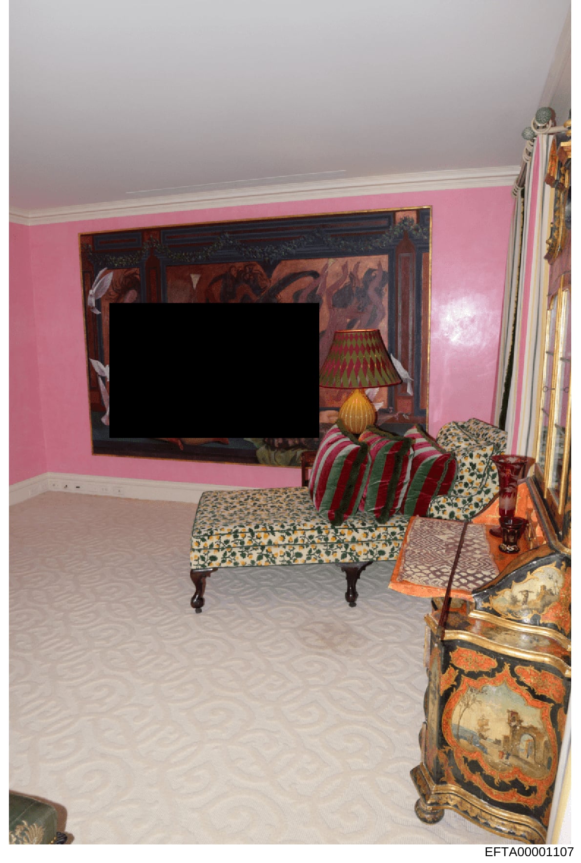 This is a photograph of an interior room featuring distinctive pink walls, a mounted flat-screen television, and ornate furnishings including decorative Asian artwork, patterned upholstered furniture, and various decorative objects. The room appears 