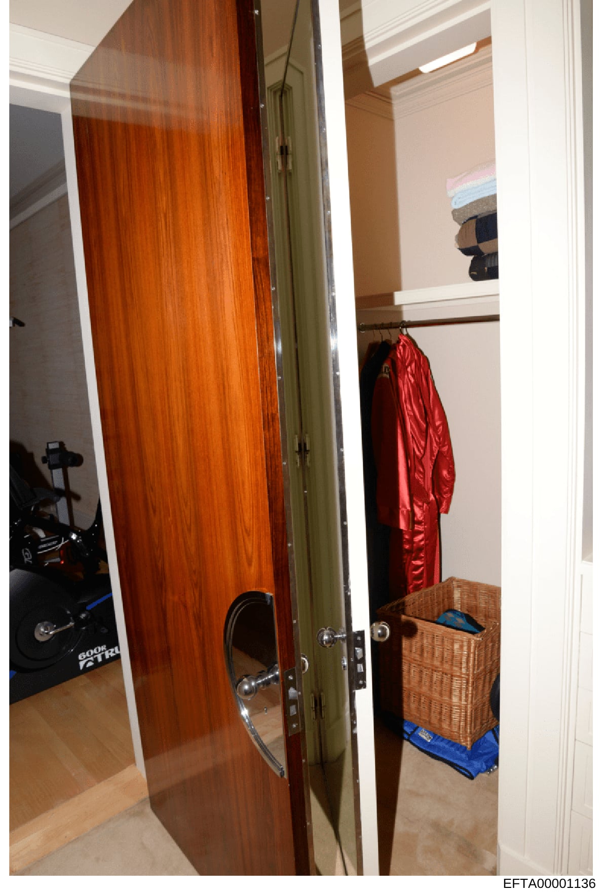 This photograph shows the interior of a walk-in closet or dressing room area, featuring exercise equipment visible on the left side, storage baskets, and clothing items including a red jacket or robe hanging on a rod. The image appears to be part of 